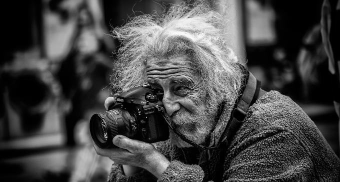 На фотографии дедушка профессиональный фотограф с седой бородой в руках у него фотоаппарат Nicon.