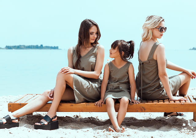 На фотографии две девушки модели и девочка ребенок, они на пляже сидят на шезлонге рекламируют платья