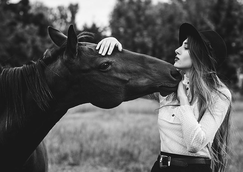 на фотографии девушка в шляпе в белой блузке с длиными волосами она обнимает за голову красивую живую лошадь