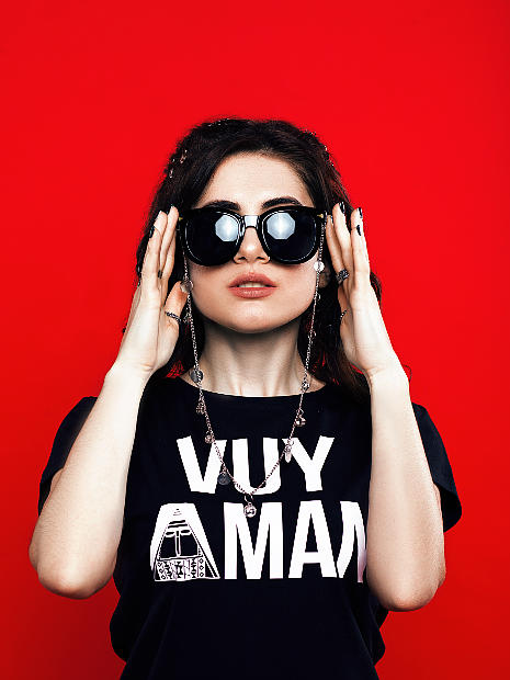 На фото девушка армянка в черных очках она руками держится за них. на ней черная футболка с надписью Vuy Aman