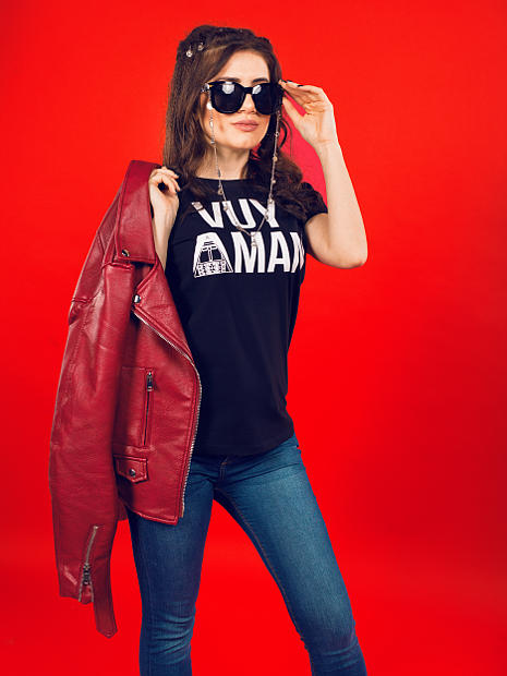 На фото девушка армянка в черных очках рукой поправляет очки. На ней черная футболка с надписью Vuy Aman и в руке красная кожаная куртка.