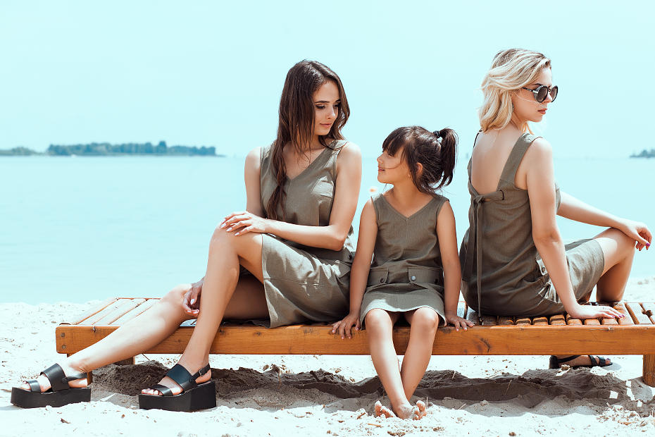На фотографии две девушки модели и девочка ребенок они рекламируют платья. Находятся они на пляже сидят на шезлонге